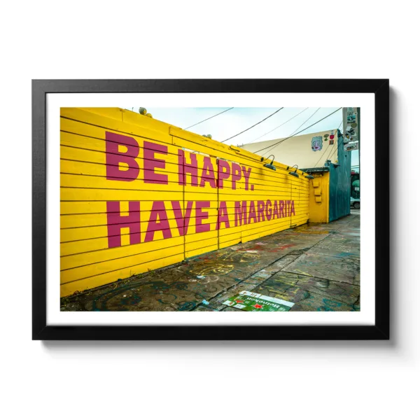 Bildaufnahme von einer gelben Wand mit dem Schriftzug "Be Happy Have a Margarita"