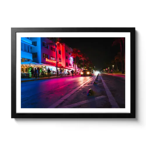 Bildaufnahme vom Ocean Drive in Miami bei Nacht. Neonlichter und ein fahrendes Auto.