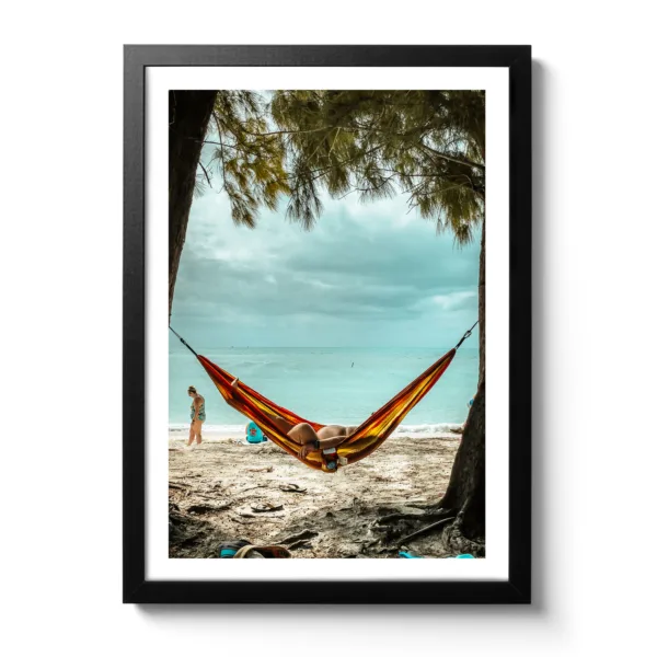 Bildaufnahme eines Mannes, der am Strand unter Palmen in einer Hängematte liegt und das Meer im Hintergrund ist. Das lustige dabei, man sieht sein kleines Bäuchlein.