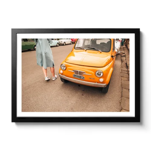 Bildaufnahme eines typischen Oldtimer Fiat in Italien. Das Auto ist knallig orange und neben an steht ein Frau in einem Kleid.